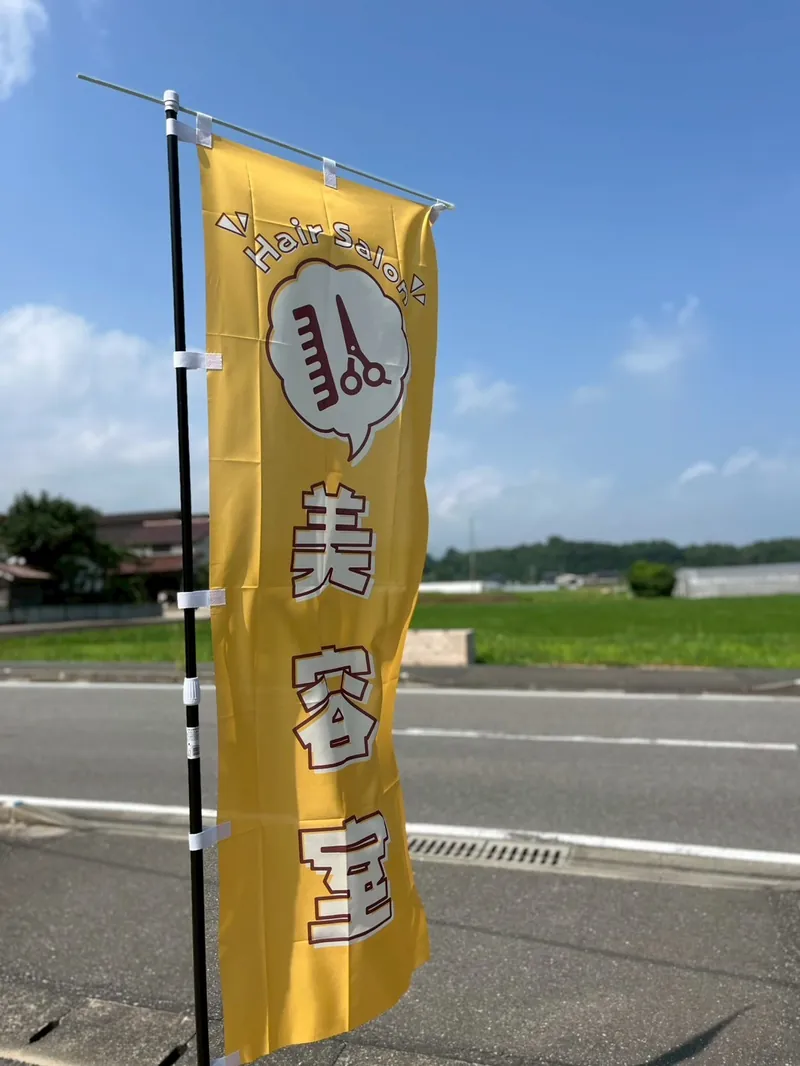 糸島市井原の道路沿いに立つ美容室ののぼり旗と青空